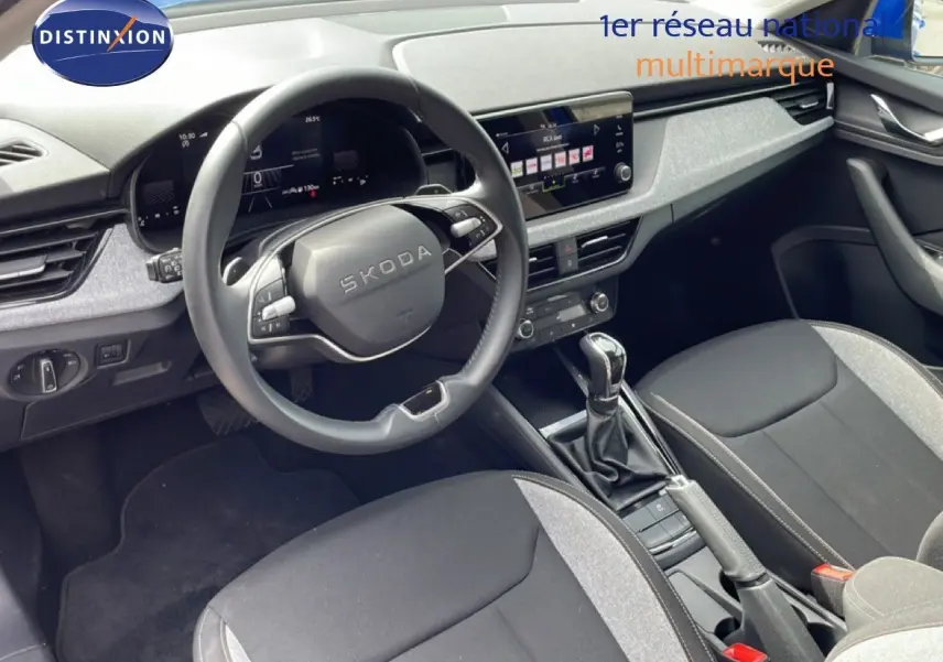 Vue intérieure côté conducteur de la Skoda Scala 2025, volant multifonction, sellerie tissu gris et noir, console centrale avec boîte auto.