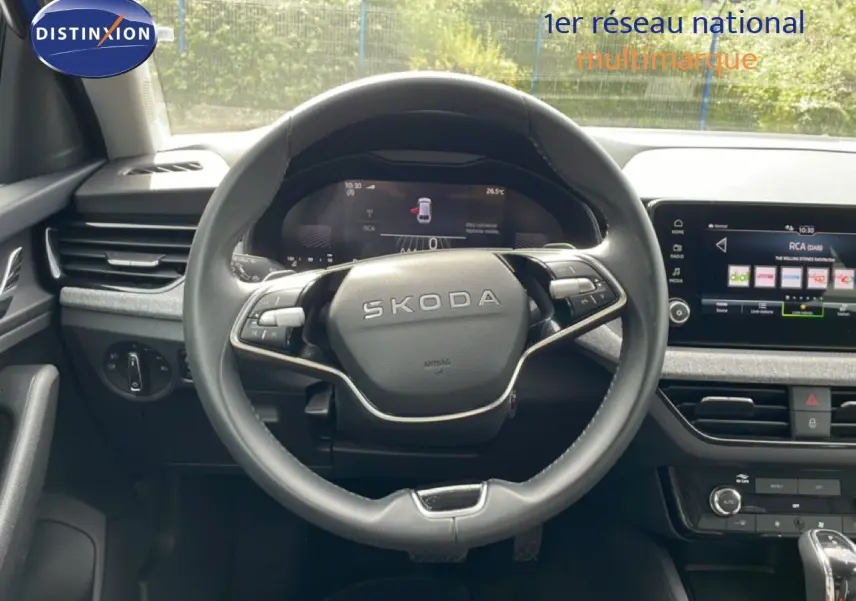 Vue intérieure centrée sur le volant SKODA d'une Scala 2025, avec tableau de bord numérique et écran tactile visible.