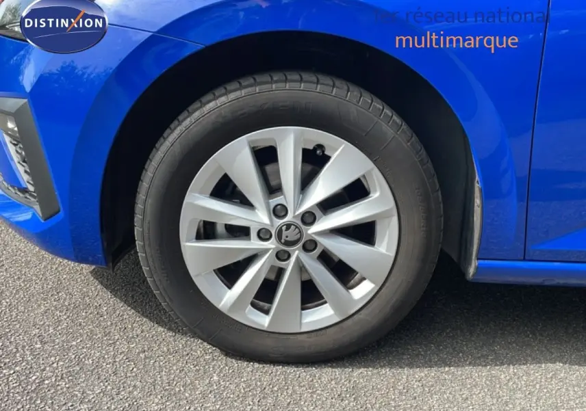 Gros plan sur la roue avant gauche d'une Skoda Scala bleu racing metal avec jante argentée et logo central visible.