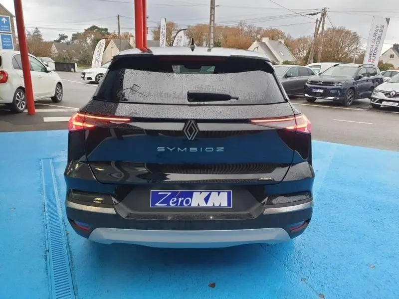 Vue arrière du Renault SYMBIOZ noir étoilé avec feux LED fins et logo centré sur un parking bleu.