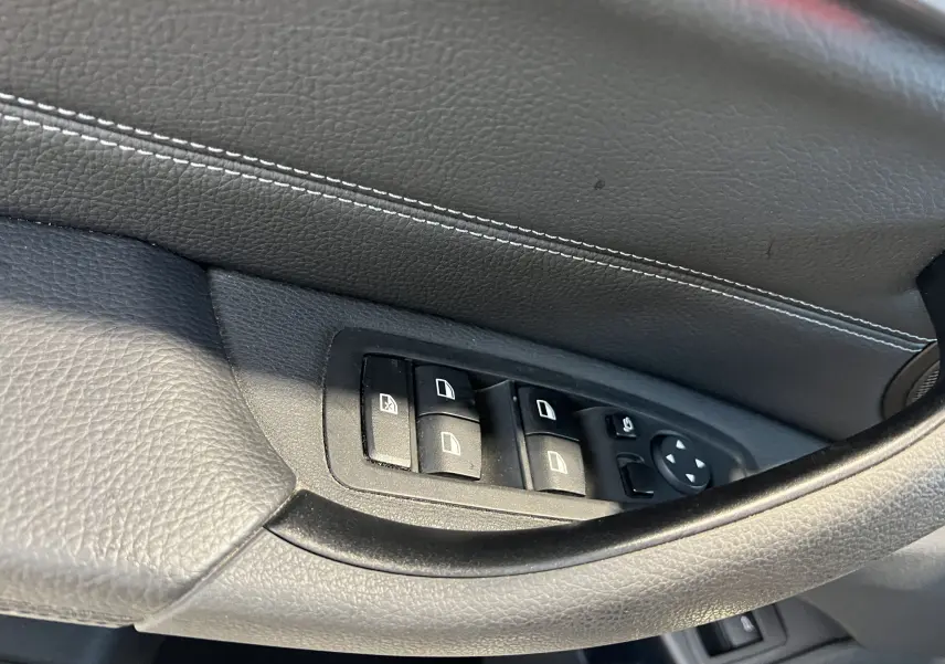 Gros plan sur les commandes des vitres côté conducteur d'un BMW X1 F48 noir avec surpiqûres blanches sur la porte.