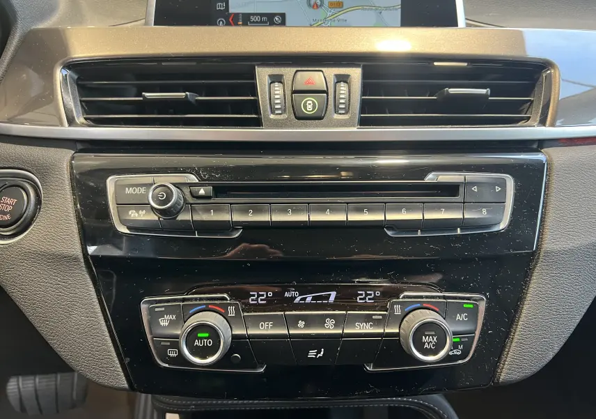 Tableau de bord intérieur de BMW X1 F48 noir, vue frontale centrée sur commandes climatisation et multimédia.