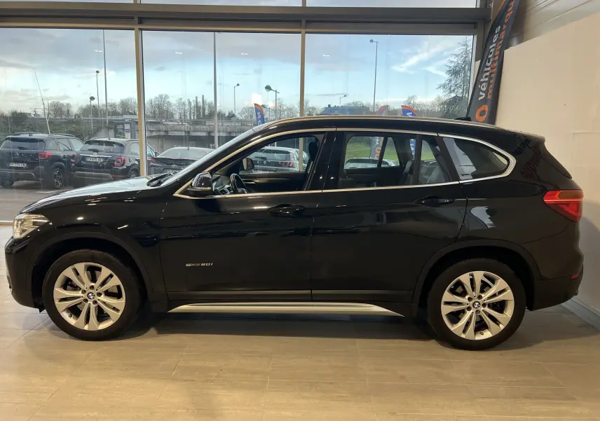 Profil côté gauche d'un BMW X1 F48 noir Saphirschwarz de 2017, finition sDrive16d Lounge, en intérieur showroom.