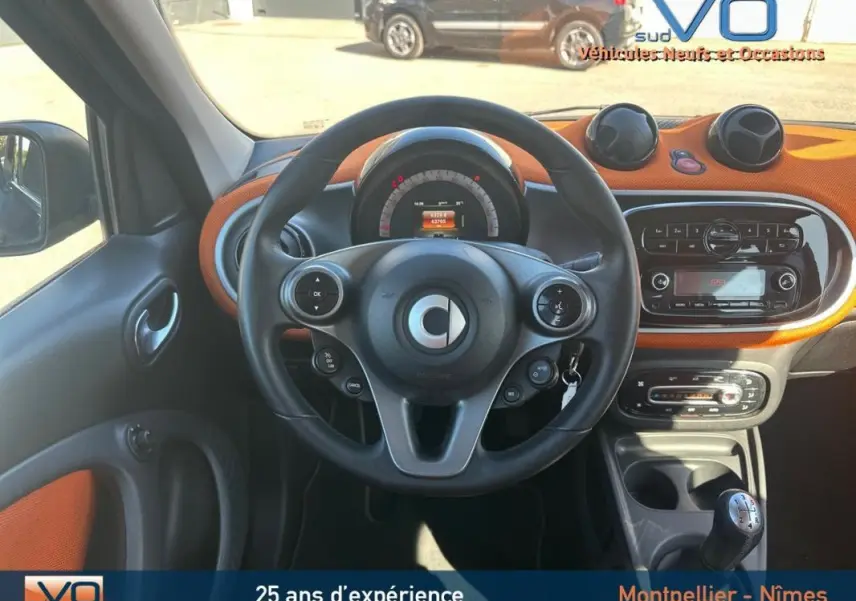 Vue intérieure centrée sur le volant multifonctions et tableau de bord orange d'une Smart Forfour noire de 2015.