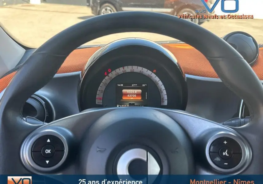 Vue depuis le volant d'une Smart Forfour noire de 2015, affichage numérique du compteur au centre du tableau de bord.