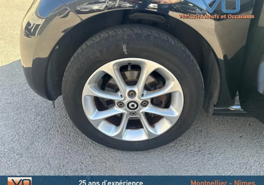 Gros plan sur la roue avant droite d'une Smart Forfour noire de 2015, mettant en valeur la jante en alliage et le logo central.