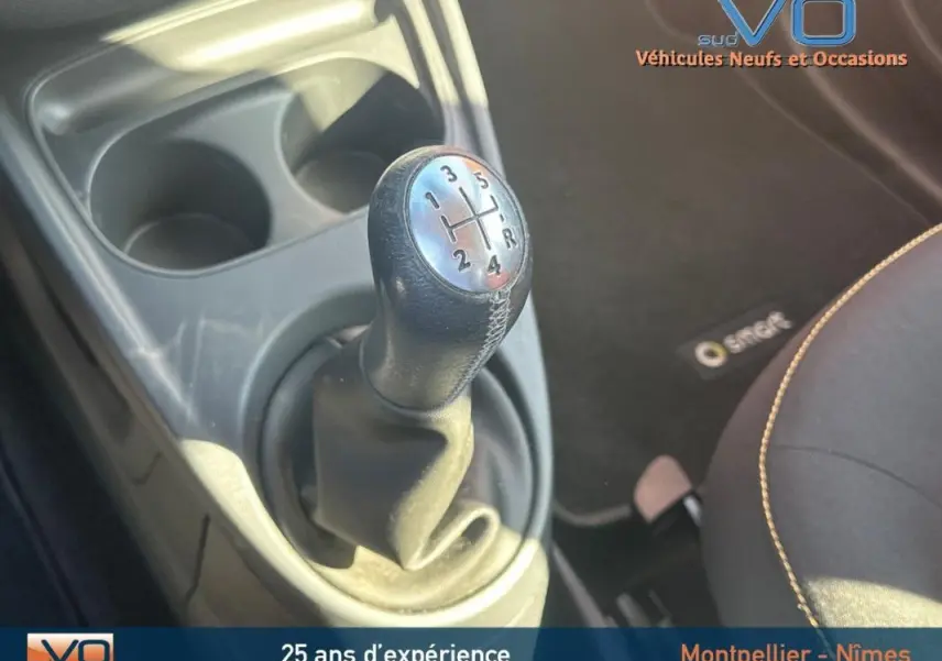 Le levier de vitesse manuel noir de la Smart Forfour 2015, avec console et porte-gobelets visibles.