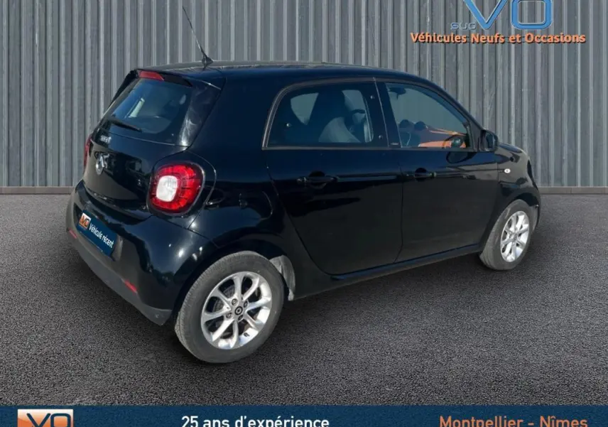 Vue 3/4 arrière droite d'une Smart Forfour noire de 2015 avec jantes argentées sur fond urbain.
