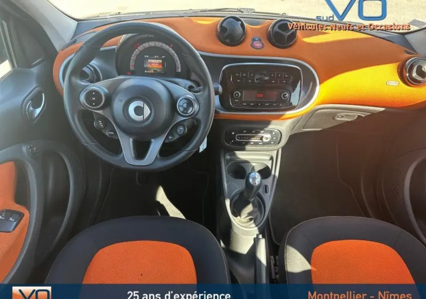 Vue intérieure avant de la Smart Forfour noire 2015, tableau de bord orange avec volant multifonctions et boîte manuelle.
