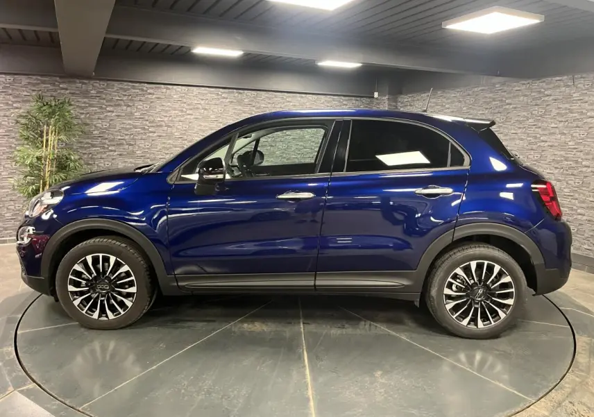 Profil côté gauche d'un Fiat 500X bleu métallisé 2024 avec jantes alliage 17 pouces et vitres surteintées.