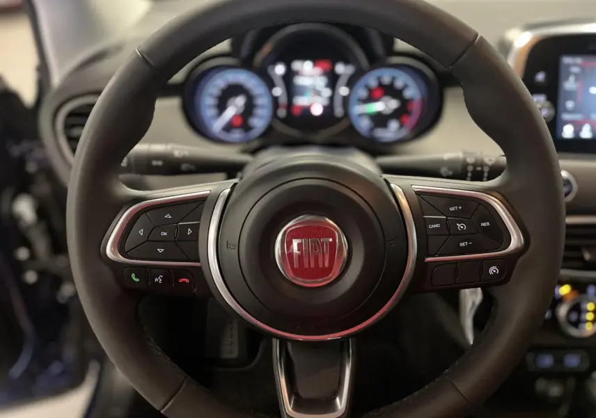 Volant Fiat 500X 2024 en cuir avec commandes intégrées, tableau de bord numérique flou en arrière-plan.