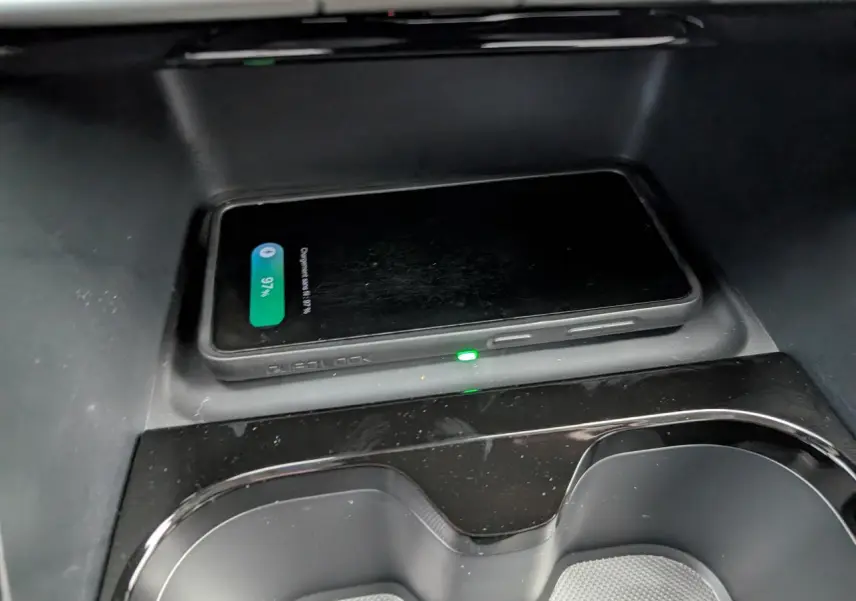 Gros plan sur la console centrale noire avec smartphone en charge sans fil dans une Citroën C3 Aircross gris métallisé.