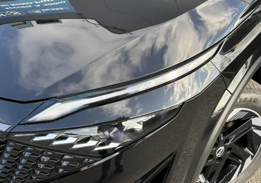 Gros plan sur le phare avant gauche noir brillant du Nissan Qashqai 2025 avec jante alliage et détails LED distinctifs.