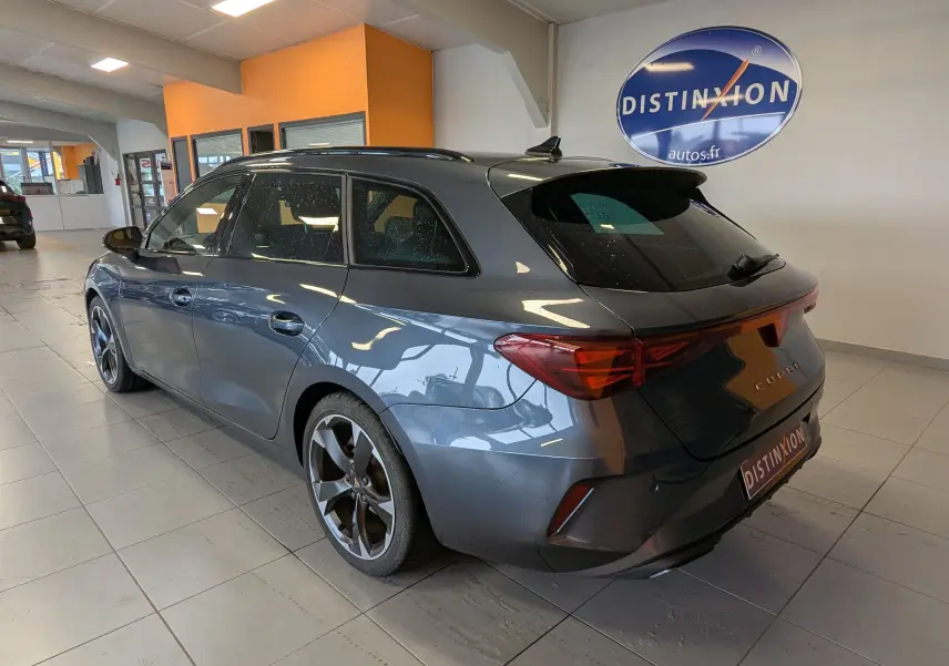 Vue 3/4 arrière droite d'une CUPRA LEON ST gris magnetic avec jantes bi-ton 18 pouces dans un showroom.