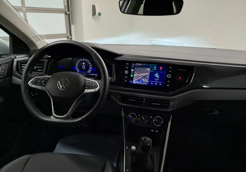 Vue intérieure du tableau de bord du Volkswagen Taigo 2025 avec volant multifonction, écran tactile et levier de vitesse manuel.