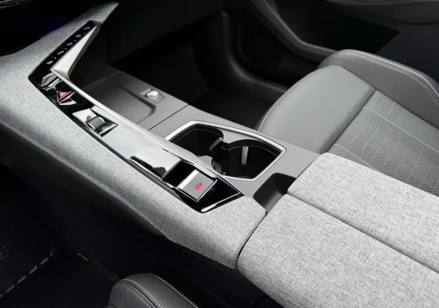 Vue rapprochée de la console centrale grise et noire du Peugeot 3008 Hybrid 145 e-DSC6 GT avec sellerie tissu et accoudoir.