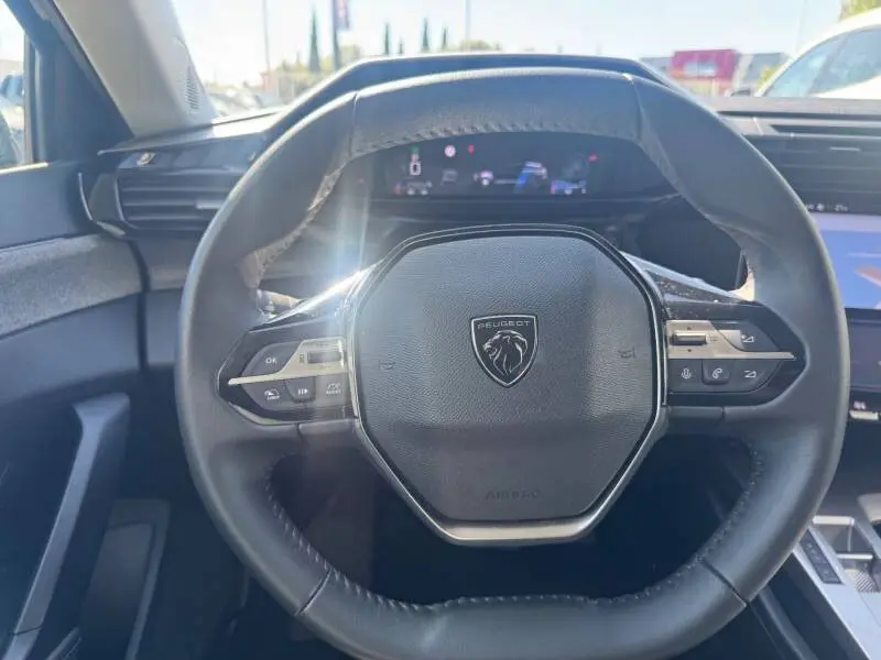 Vue rapprochée du volant noir du Peugeot 308 Hybrid 145 e-DCS6 Allure 2025 avec tableau de bord numérique en arrière-plan.