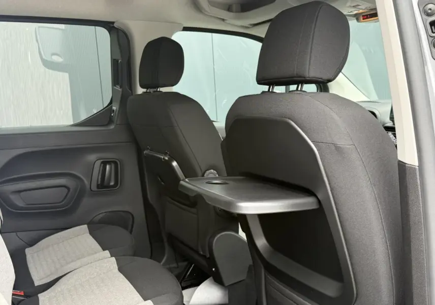 Vue intérieure arrière droite du Citroën Berlingo gris acier montrant les sièges avec tablette rabattable et lunette arrière ouvrante.