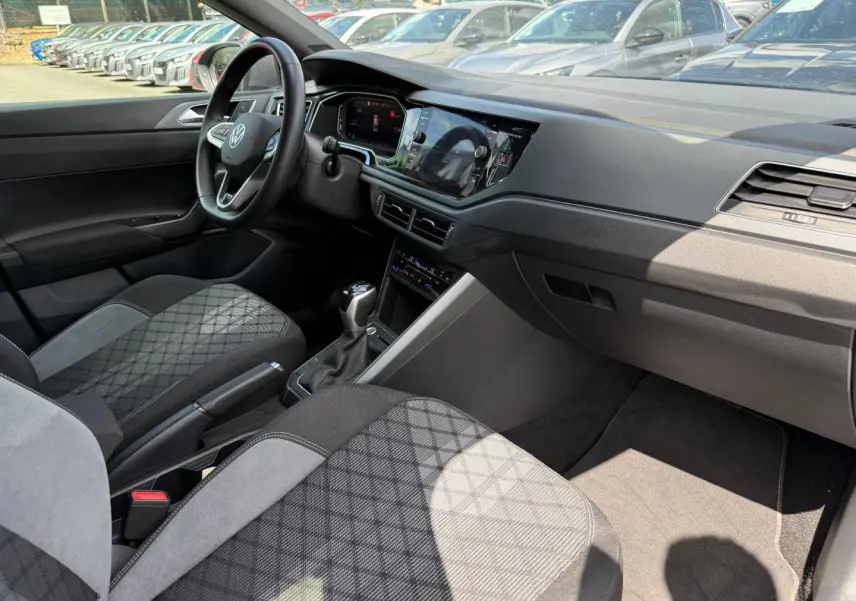 Vue intérieure côté passager avant du Volkswagen Taigo 2025, montrant le tableau de bord et les sièges en tissu gris à motif.