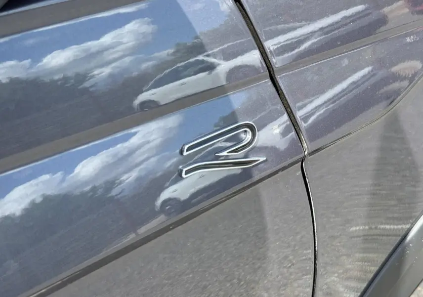 Détail du logo R-Line sur la porte côté gauche d’un Volkswagen Taigo gris Ascot 2025.