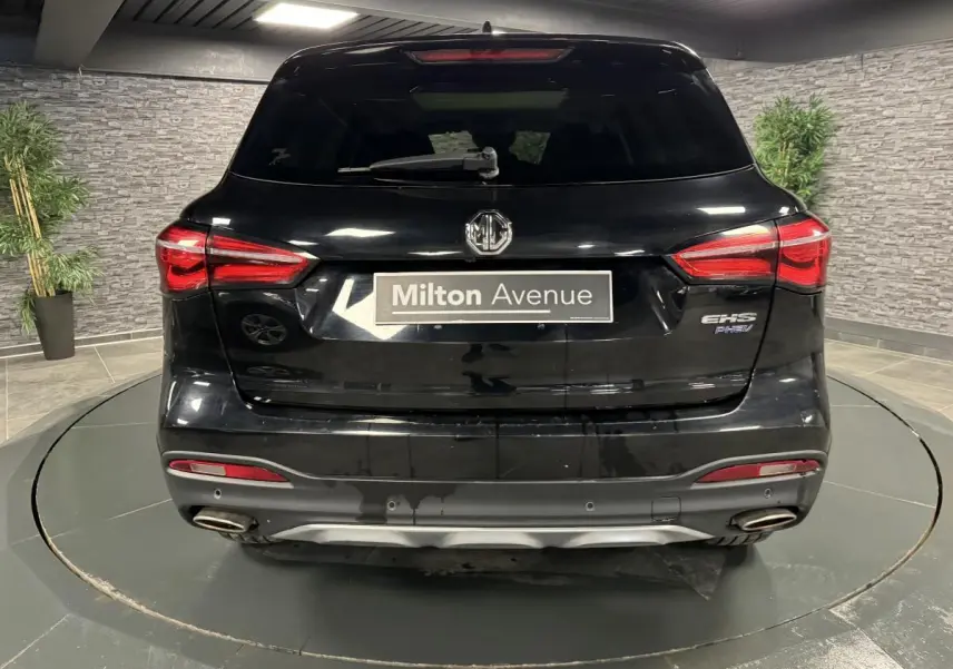 Vue arrière du SUV MG Motor EHS noir métallisé avec feux LED et double sorties d'échappement visibles en intérieur showroom.