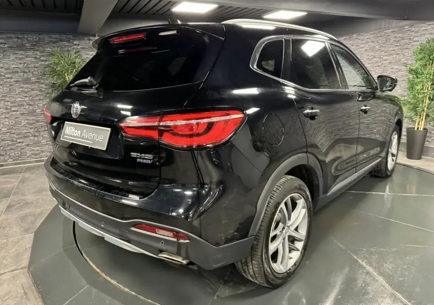 Vue 3/4 arrière droite du MG MOTOR EHS noir métallisé avec feux arrière LED et jantes alliage 18 pouces dans un showroom.