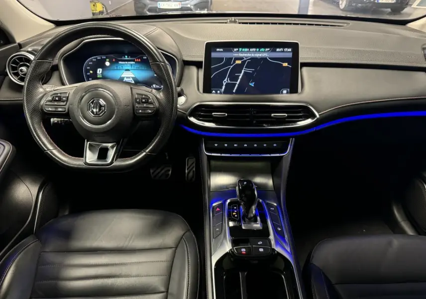 Vue intérieure avant du tableau de bord et console centrale du MG MOTOR EHS noir avec écran tactile et éclairage d'ambiance bleu.