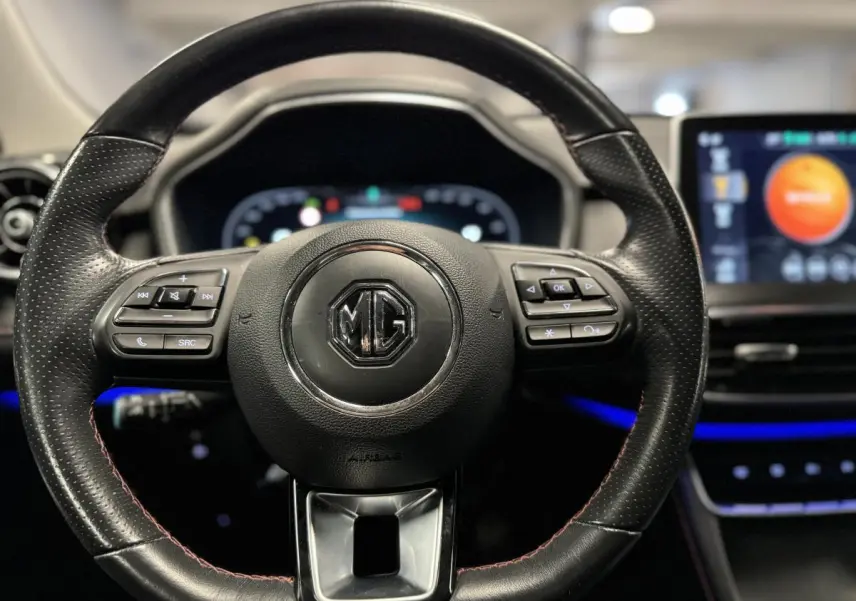 Volant cuir noir perforé avec logo MG au centre, tableau de bord numérique et écran tactile lumineux en arrière-plan