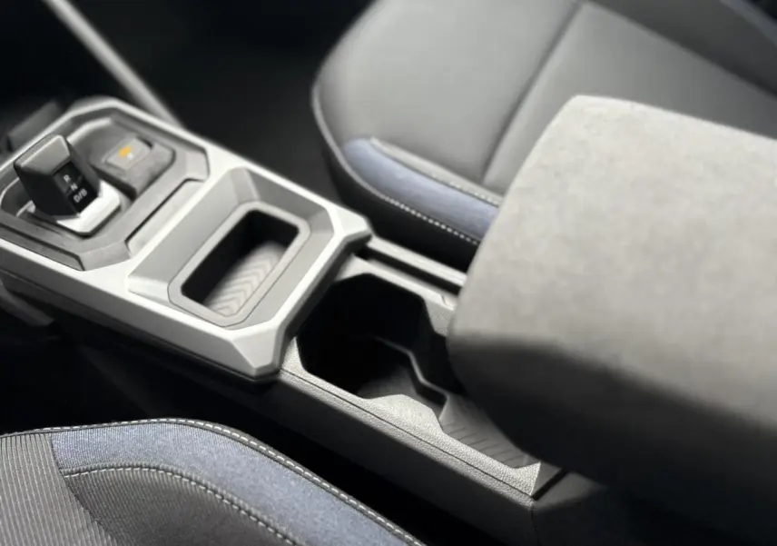 Gros plan sur la console centrale et le levier de vitesse du Dacia Duster blanc Glacier, avec accoudoir et sièges tissu noir et bleu.