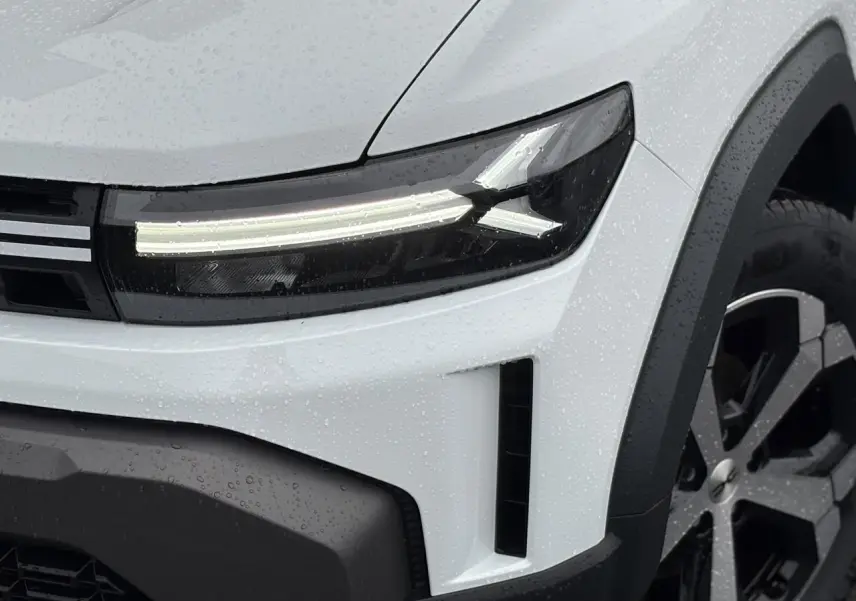 Gros plan sur l'avant droit du Dacia Duster blanc Glacier, mettant en valeur le phare LED et la jante alliage noire.