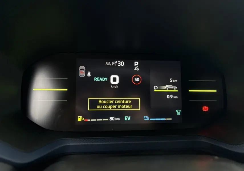 Tableau de bord digital du Dacia Duster 2025 affichant vitesse, autonomie et alertes de sécurité en mode hybride.