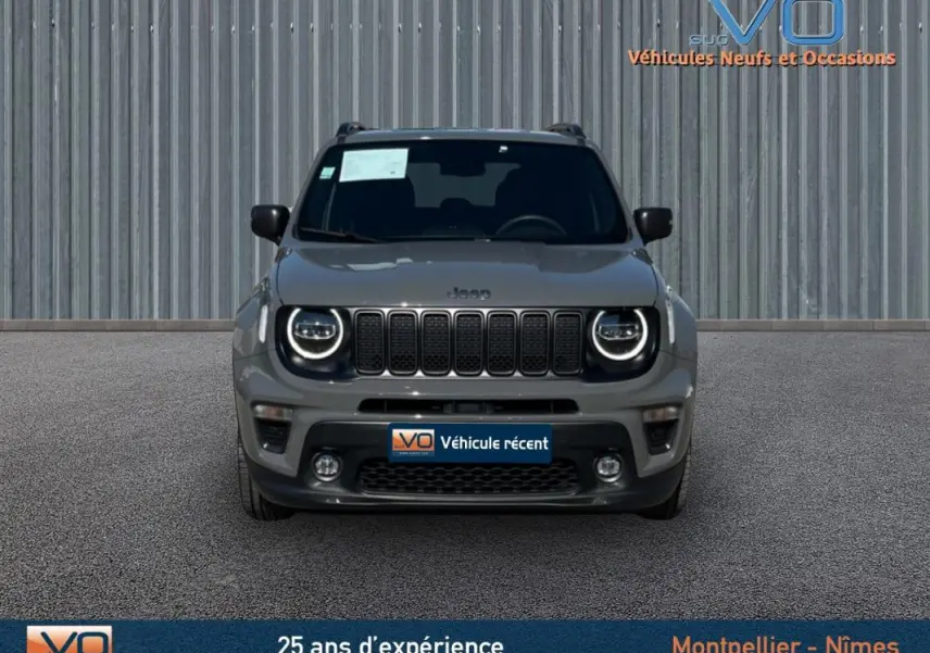 Vue frontale d'un Jeep Renegade gris foncé avec phares LED ronds et barres de toit visibles sur fond urbain.