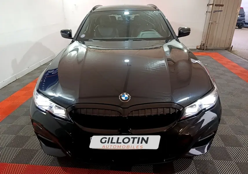 BMW Série 3 318i M Sport noir vue de face en intérieur avec calandre noire et phares LED allumés.