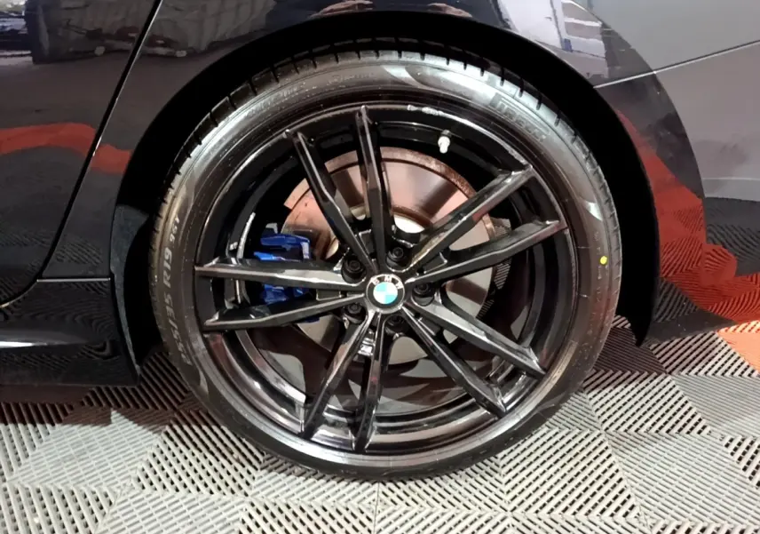 Gros plan sur la roue arrière droite noire d'une BMW Série 3 318i M Sport avec étrier de frein bleu visible.