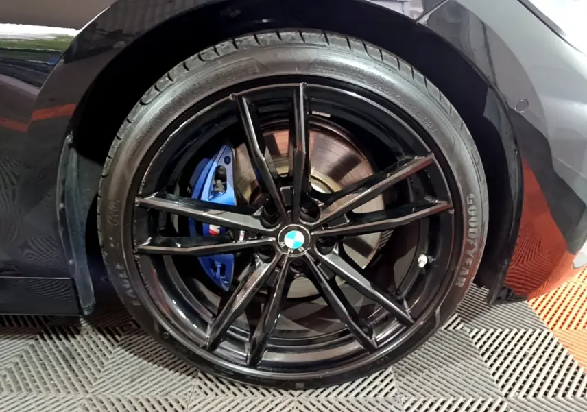 Gros plan sur la roue arrière droite noire d'une BMW Série 3 318i avec étrier de frein bleu M Sport visible.