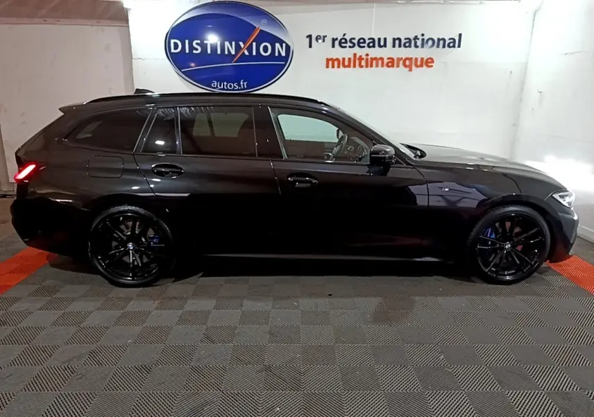 BMW Série 3 318i M Sport noir vue de profil côté gauche, avec jantes noires et feux arrière allumés.
