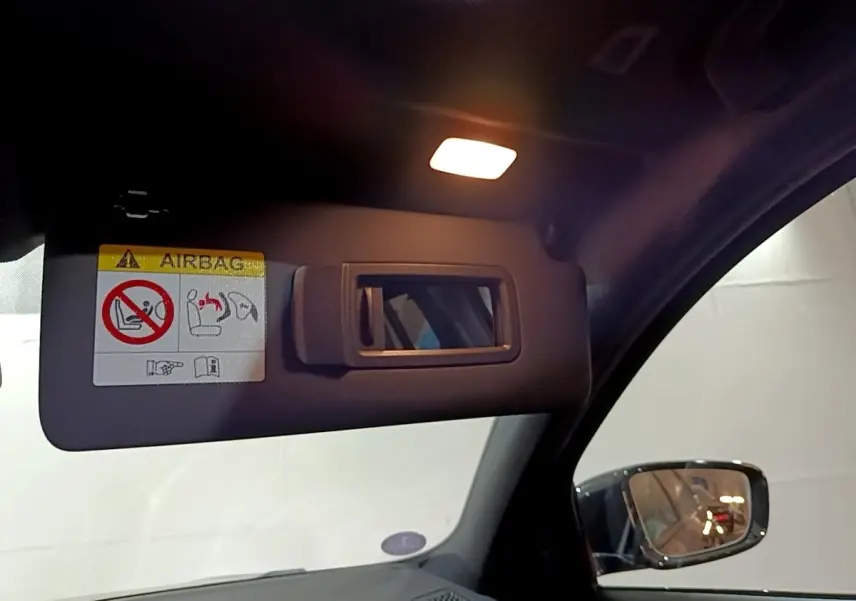 Détail du pare-soleil côté conducteur avec miroir et avertissement airbag dans une BMW Série 3 noire 2022.