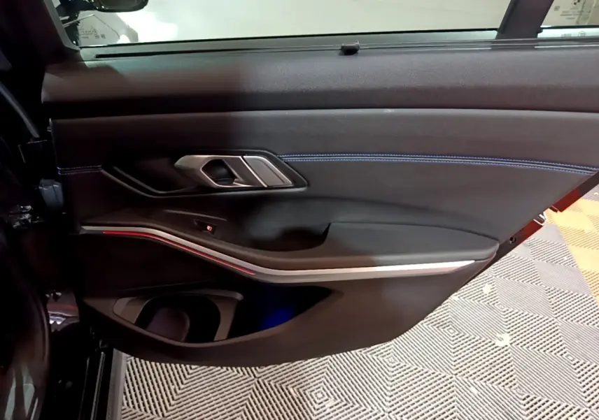 Vue rapprochée de la porte intérieure côté gauche noire de la BMW Série 3 318i M Sport avec éclairage d'ambiance rouge.