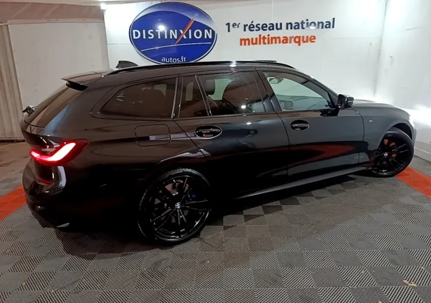 BMW Série 3 318i M Sport noir vue de profil côté gauche en intérieur avec jantes noires et feux arrière allumés