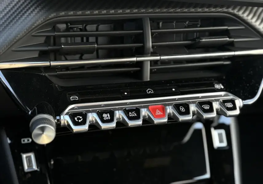 Gros plan sur la console centrale noire du Peugeot 2008 Hybrid 145, montrant les commandes chromées et un bouton rouge d’alerte.