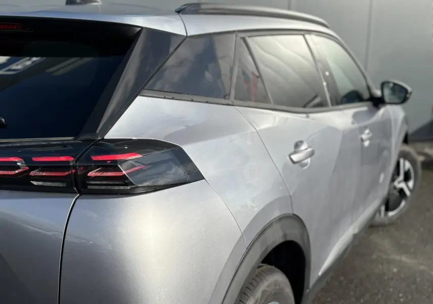 Vue 3/4 arrière droit d'un Peugeot 2008 Hybrid 145 gris Artense avec feux arrière LED 3 griffes et vitres surteintées.