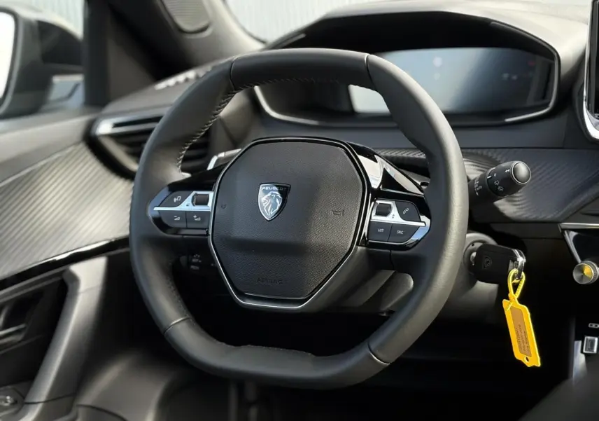 Vue rapprochée du volant compact cuir noir de la Peugeot 2008 Hybrid 145 e-DSC6 Allure avec tableau de bord numérique.