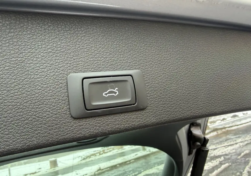 Bouton d'ouverture électrique du coffre sur le hayon intérieur d'un Audi Q2 gris aluminium, vue rapprochée.