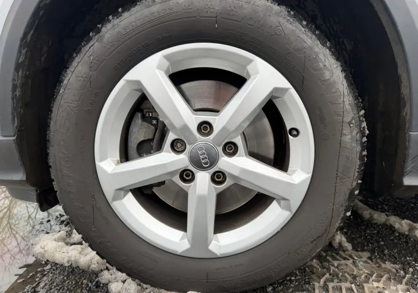 Gros plan sur la roue avant droite d'un Audi Q2 gris aluminium, avec jante alliage 5 branches et pneu hiver Dunlop.
