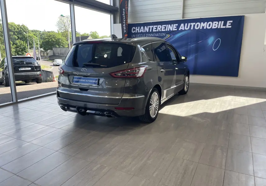 Vue 3/4 arrière droite d'un Ford S-MAX Vignale gris magnetic 2022 en showroom avec logo Vignale visible.
