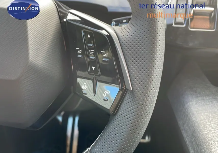 Gros plan sur le volant perforé d'une Peugeot 3008 hybride 2025, avec commandes intégrées et intérieur sombre.