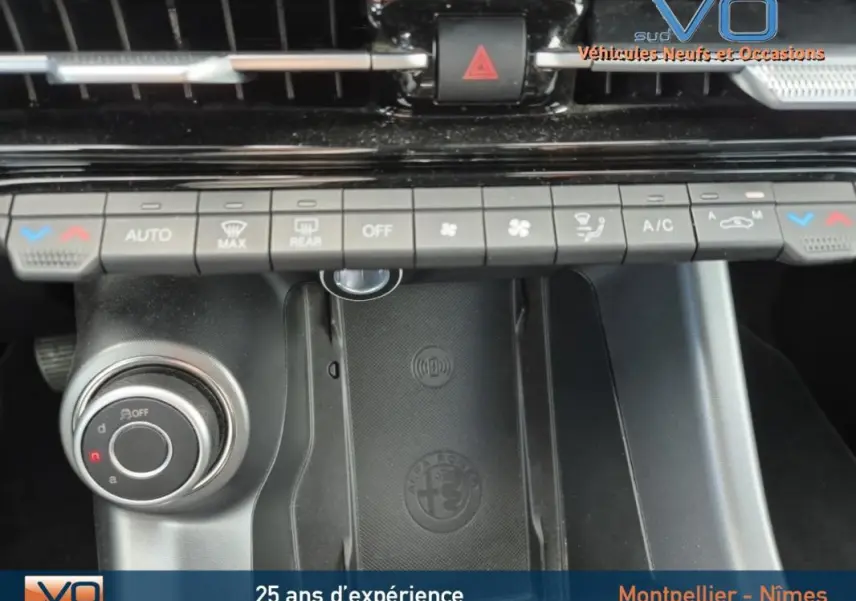 Vue rapprochée de la console centrale de l'Alfa Romeo Tonale 2023, montrant les commandes de climatisation et le chargeur sans fil noir avec logo Alfa Romeo.