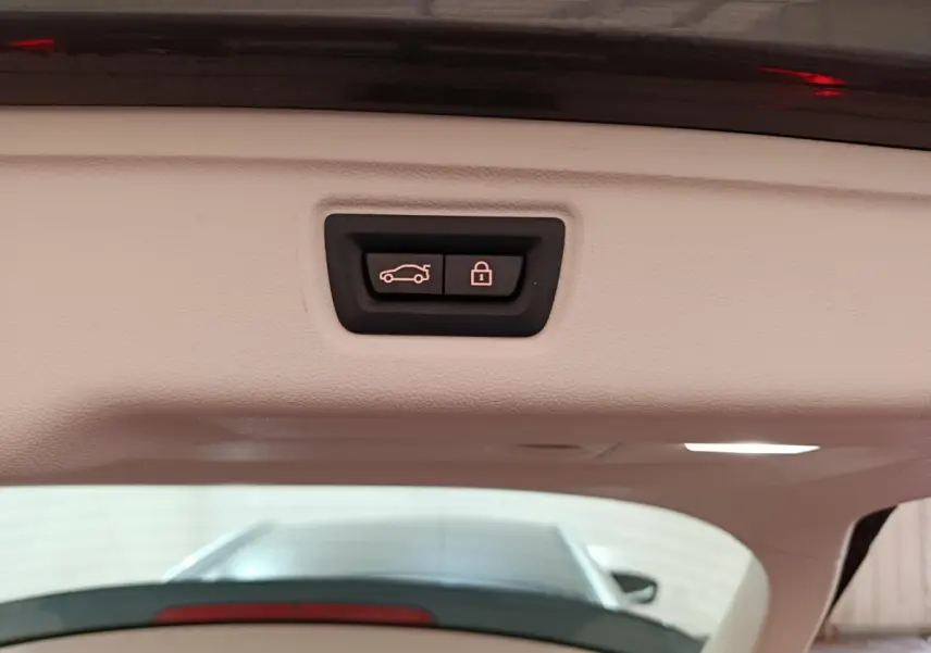 Bouton d'ouverture et de verrouillage électrique du coffre sur le hayon intérieur d'une BMW Série 3 gris clair.