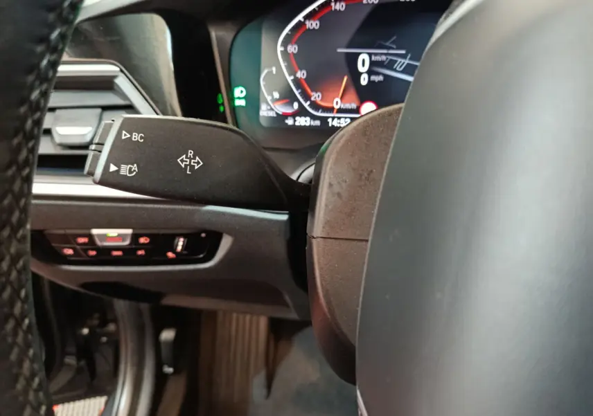 Gros plan sur le levier de clignotant et le tableau de bord numérique d'une BMW Série 3 gris clair, intérieur moderne.