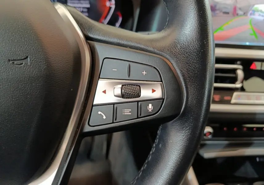 Gros plan sur les commandes du volant à droite de la BMW Série 3 316d gris clair, avec écran tactile et caméra de recul visible.